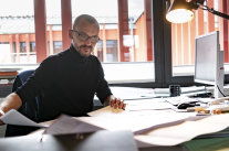 Ein Mann mittleren Alters sitzt am Schreibtisch über Dokumenten